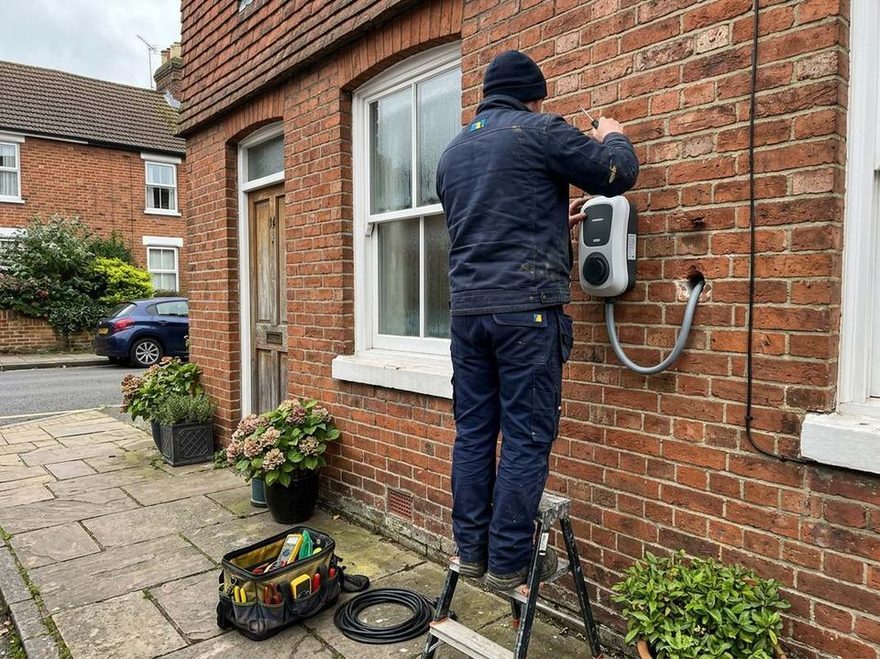 OZEV approved installer fitting a home EV charger to an outside wall